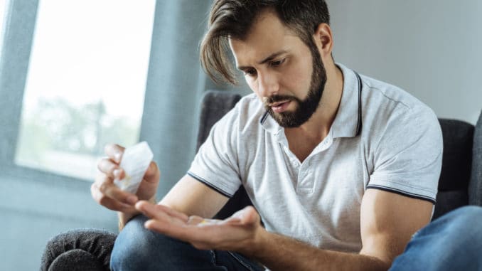 Strong antidepressants. Cheerless sad unhappy man sitting in the armchair and taking medicine while suffering from depression