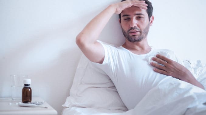 Sick man in bed measuring temperature and feeling bad Sick man in bed