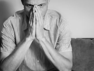 Young handsome man in the shirt cover his face with his hands feeling depressed and miserable while he thinking about life