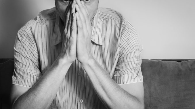 Young handsome man in the shirt cover his face with his hands feeling depressed and miserable while he thinking about life