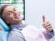 Portrait of smiling man showing thumbs up while sitting on chair at dentist clinic