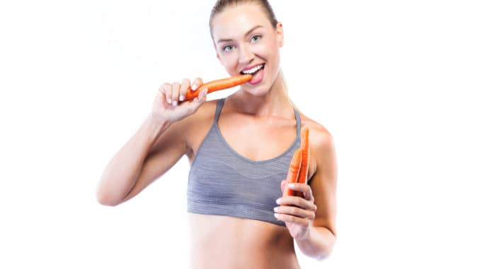 Portrait of beautiful young woman eating carrots over white background.