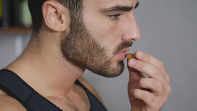 Young athletic man eating almonds in kitchen, choosing a healty lifestyle