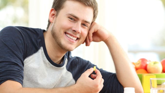 Happy man holding omega 3 vitamin pill on a table at home with a colorful background