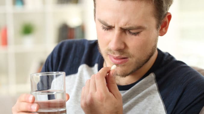 Man suffering taking a pill sitting on a sofa in the living room in a house interior