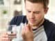 Man suffering taking a pill sitting on a sofa in the living room in a house interior