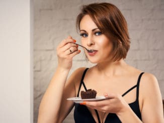 Attractive woman eating chocolate cake at home on couch