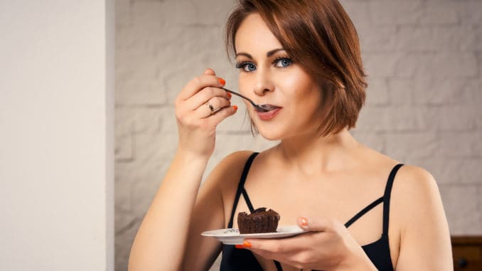 Attractive woman eating chocolate cake at home on couch