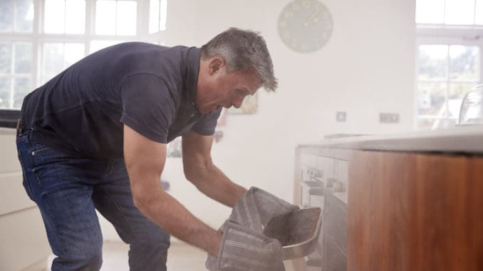 Middle aged man opening smoke filled oven in the kitchen