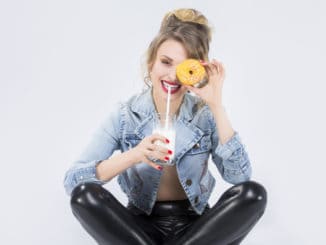 Food Ideas and Concepts. Young Caucasian Blond Girl Having Fun with Cup of MIlk and Donut Bagel. Drinking Milk Through Straw