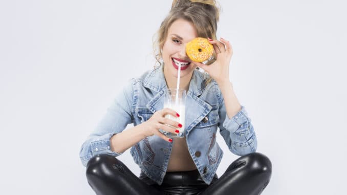 Food Ideas and Concepts. Young Caucasian Blond Girl Having Fun with Cup of MIlk and Donut Bagel. Drinking Milk Through Straw
