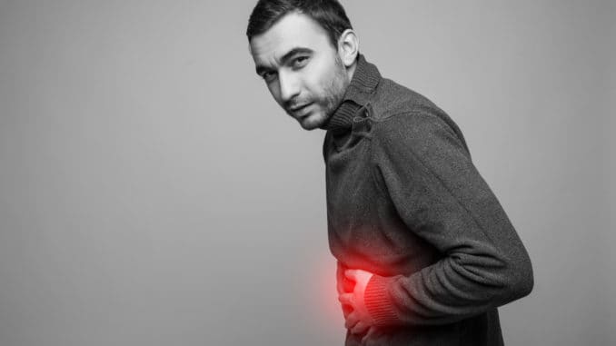 young man holding his sick stomach in pain, isolated on gray background, monochrome photo with red as a symbol for the hardening Young man holding his sick stomach in pain