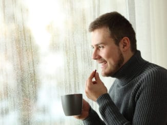 man taking a pill looking through a window