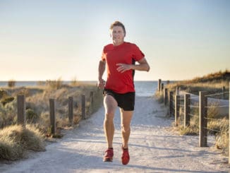 Young attractive and happy sport runner man with fit and strong healthy body training on off road track in Summer running workout under Summer sun in health care and competition concept