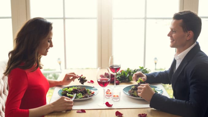 dreamstime_m_109149325 Young men and women having romantic dinner in the restaurant eating salad enjoying food