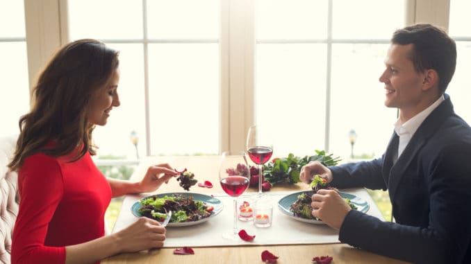 Young men and women having romantic dinner in the restaurant eating salad enjoying food