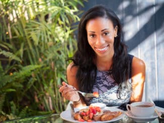 Beautiful dark skinned girl with a broad charming smile having breakfast with french toasts, fruits and berries.