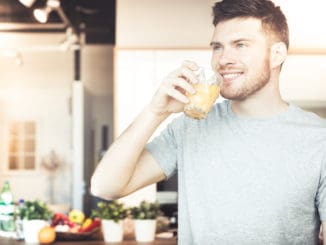 Handsome young man drinking orange juice in kitchen in the morning