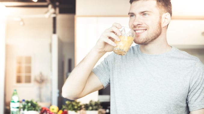 Handsome young man drinking orange juice in kitchen in the morning
