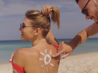 Happy couple applying sun tanning lotion on the beach, men putting sunscreen suntan cream on woman