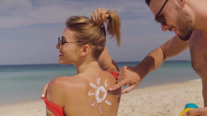 Happy couple applying sun tanning lotion on the beach, men putting sunscreen suntan cream on woman