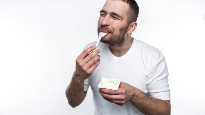 Young and strong man is eating yogurt.