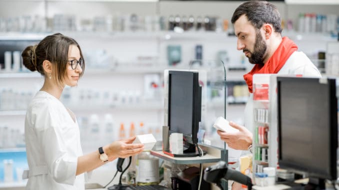 Man buying medication standing with pharmacist at the counter of the pharmacy store