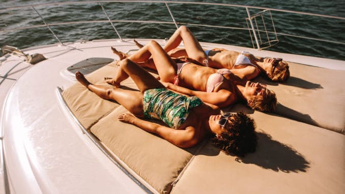 Three women in swimsuits lying and sunbathing on the bow of a luxury yacht