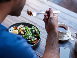 Young man sitting alone at a bistro table eating a delicious plate of mixed salad and drinking a cup of tea