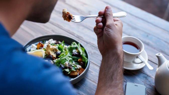 Young man sitting alone at a bistro table eating a delicious plate of mixed salad and drinking a cup of tea