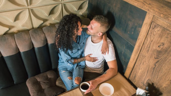 Happy young couple is drinking coffee and smiling while sitting at the cafe.