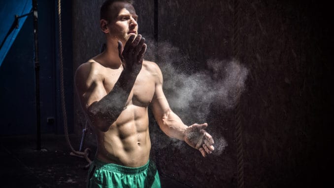 Shirtless man using chalk or magnesium powder in gym