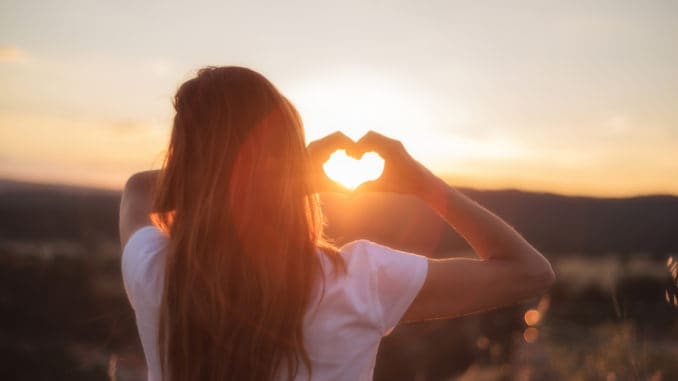 Love sign. Woman making heart with her hands at sunset .
