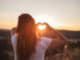 Love sign. Woman making heart with her hands at sunset .