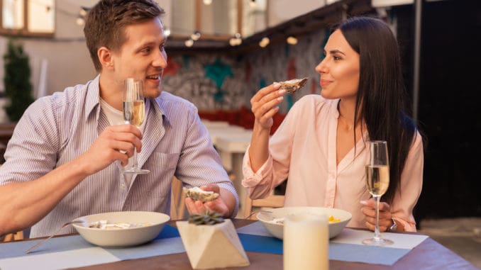 Blonde-haired man. Blonde-haired elegant men inviting her appealing women for drinking champagne and eating oysters