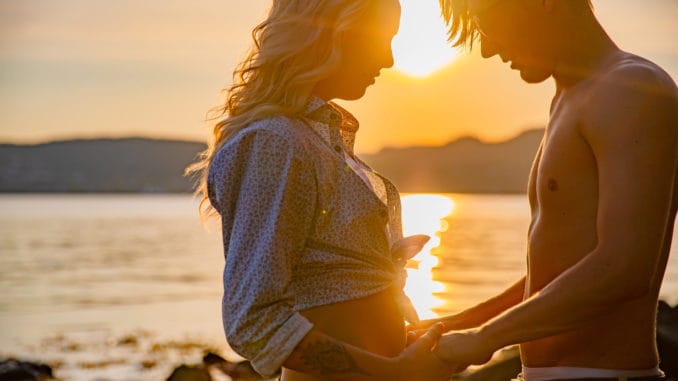 Silhouette of smiling couple in love embrace each other at the beach against sun. Summer flirt in shorts and bikini.