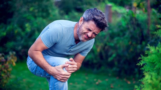 People, healthcare and problem concept - close up of an unhappy man suffering from pain in leg or knee outdoor