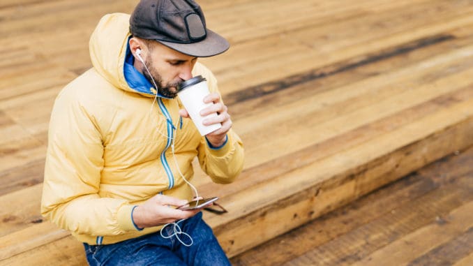 dreamstime_m_125166327 drinking delicious coffee and listening to music with earphones holding mobile phone