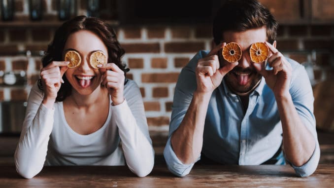 Beautiful Young Couple Having Fun in Kitchen. Handsome Smiling Woman and Man Having Fun with Colourful Oranges in Loft Kitchen. Family Preparing Dinner.