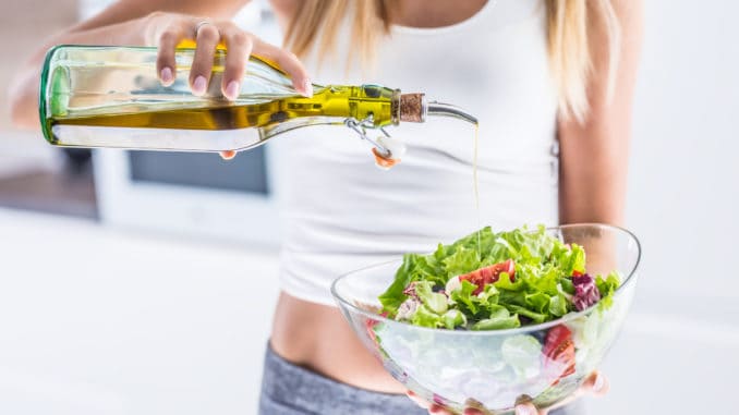Young attractive woman pouring olive oil in to the fresh vegetable salad.