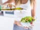 Young attractive woman pouring olive oil in to the fresh vegetable salad.