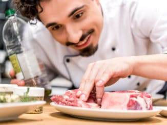 smiling chef adding oil to raw meat