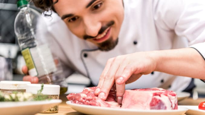 smiling chef adding oil to raw meat