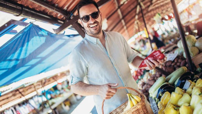 Young man consumer at an open street market buying fruits and vegetables