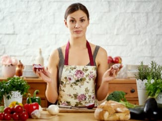 Beautiful young woman, brunette holds onions and garlic in the kitchen at a table full of organic vegetables