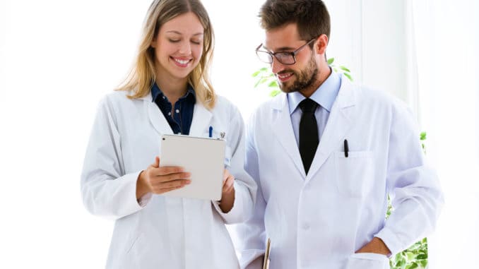 Shot of smiling young doctors looking medical reports in digital tablet in medical office