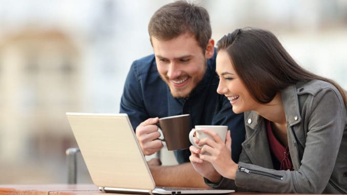 Happy couple checking laptop content on a balcony