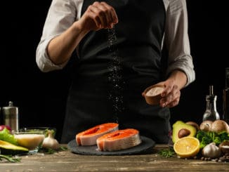 The chef prepares fresh salmon fish, smorgu trout, sprinkling salt with the ingredients.