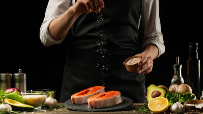 The chef prepares fresh salmon fish, smorgu trout, sprinkling salt with the ingredients.