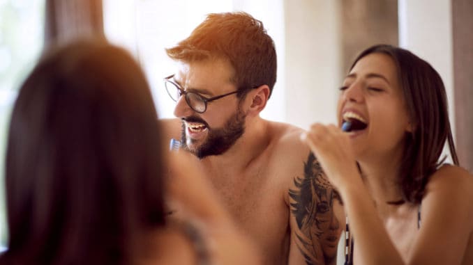 Happy men and women brushing their teeth in the bathroom